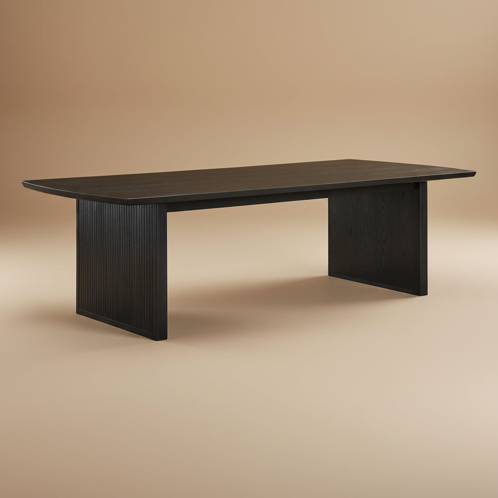 Black extension leaf dining table at an angle on a tan studio backdrop, showing fluted panel legs