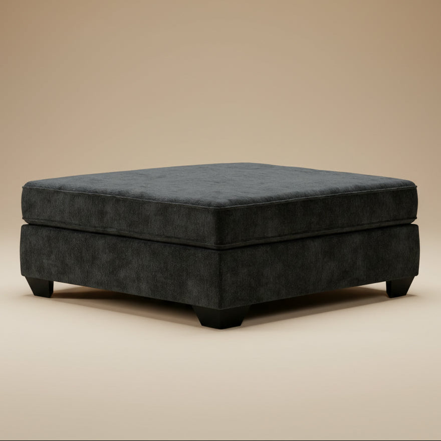 A square ottoman upholstered in dark charcoal gray velvet, shown from a three-quarter angle against a solid beige studio background.