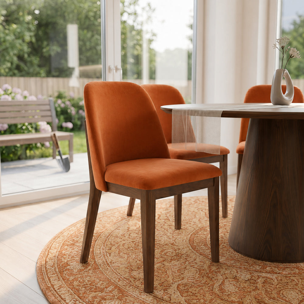 Close-up of a burnt orange velvet dining chair beside a round table with a garden view behind