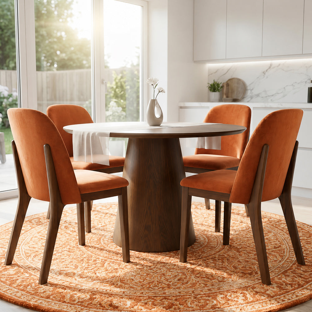 Dining chairs set around a dark wood pedestal table in a sunlit white kitchen with a round rug