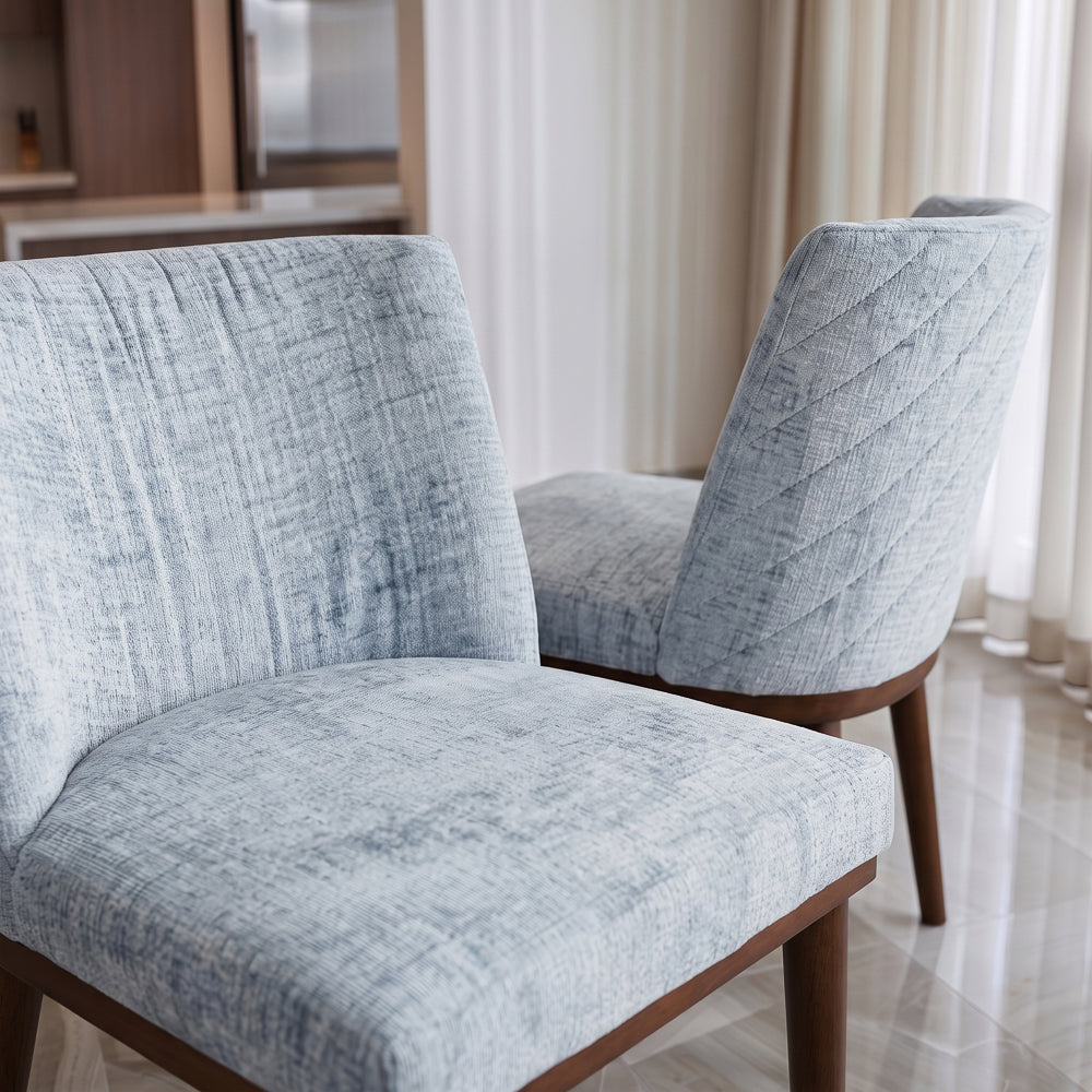 Close-up of two grey dining chairs showing seat cushion and diagonal-stitched back panel