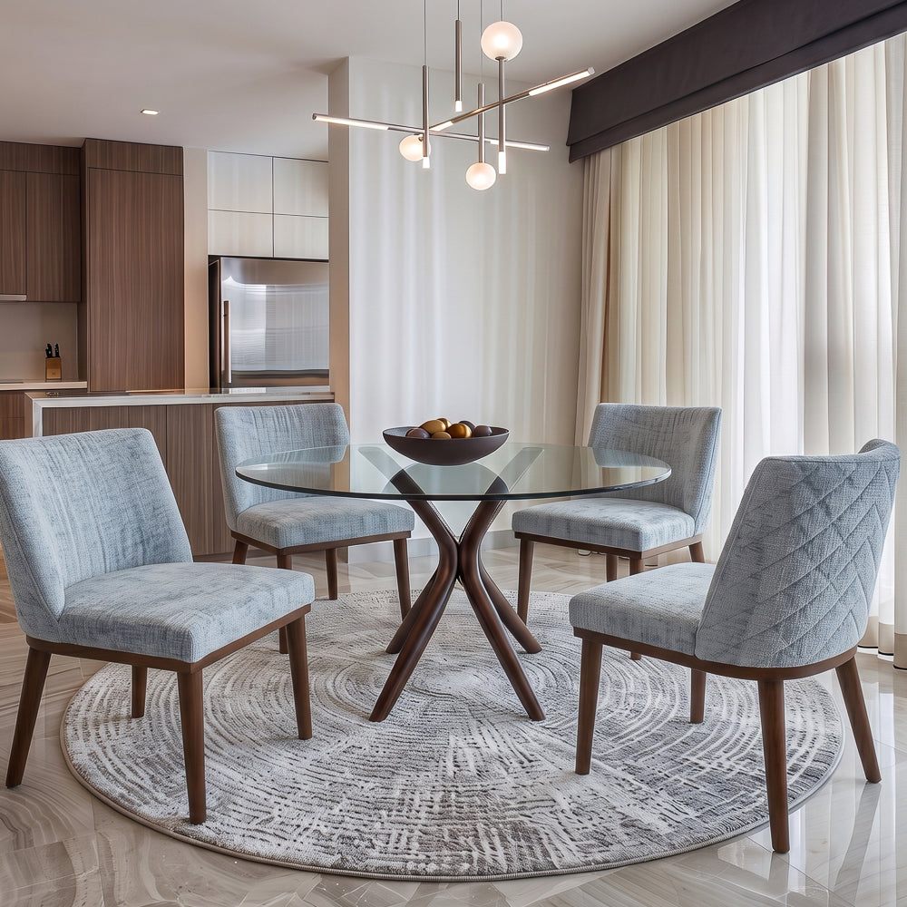Round glass dining table with four grey dining chairs on a circular rug in a modern kitchen
