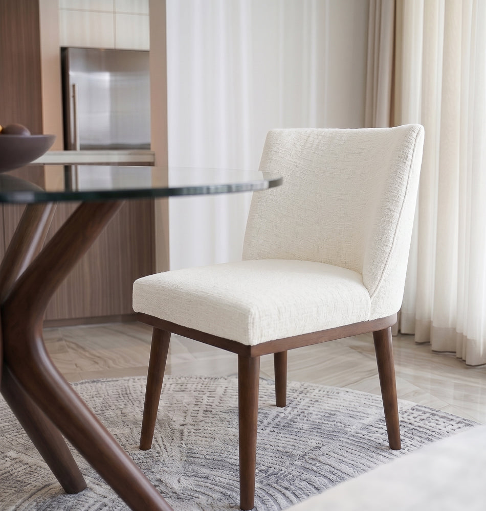 White dining chair angled next to a round glass table by sheer floor-length curtains