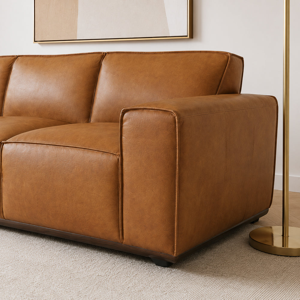 Close-up of the arm corner, piped stitching and dark wood plinth base on the leather sofa