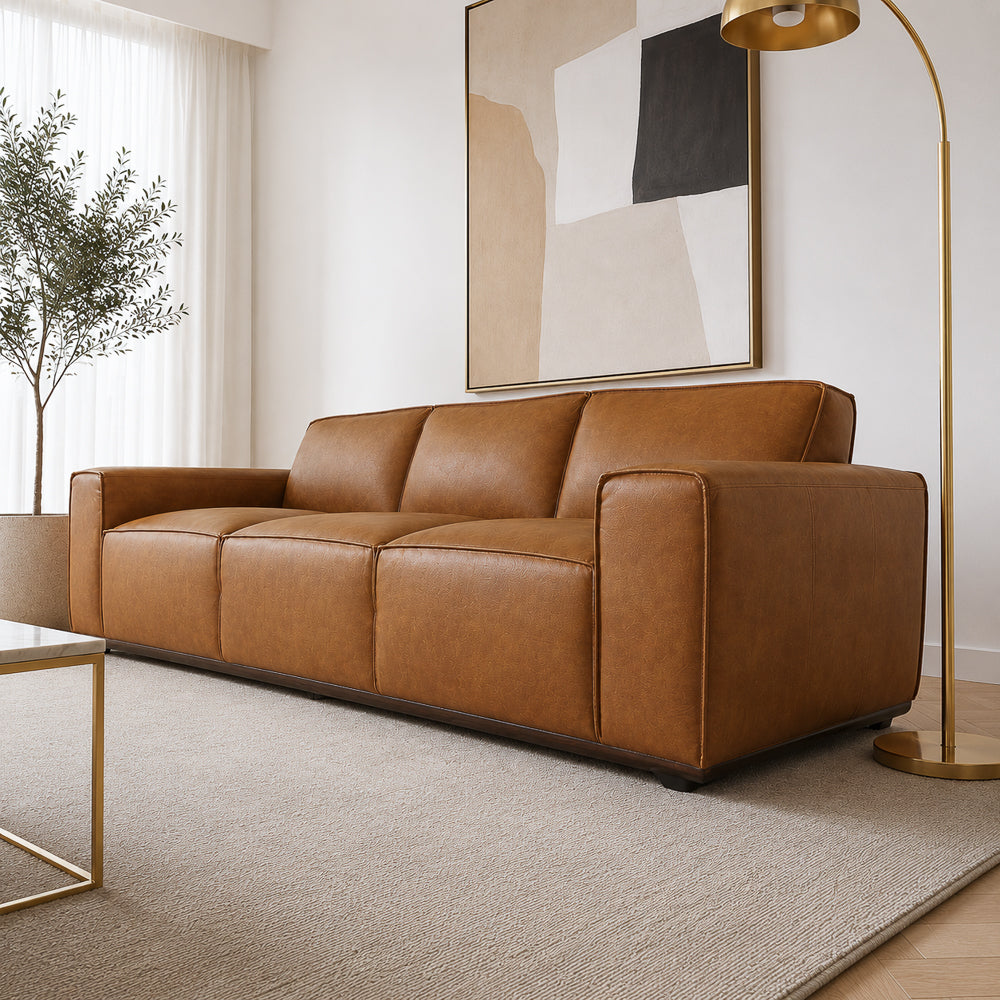 Low three-quarter angle showing the wide track arms and seat depth of the tan leather sofa