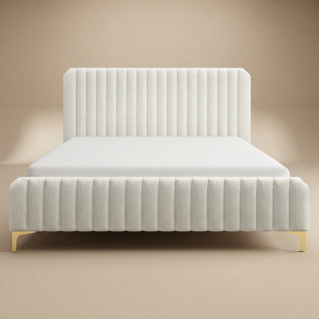 A modern white upholstered bed with a tall vertically channel-tufted headboard and matching channel-tufted footboard, supported by slim gold metal legs, shown against a warm beige studio background.