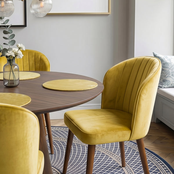 Gold velvet dining chairs pulled up to a round walnut table set with placemats and a vase of flowers