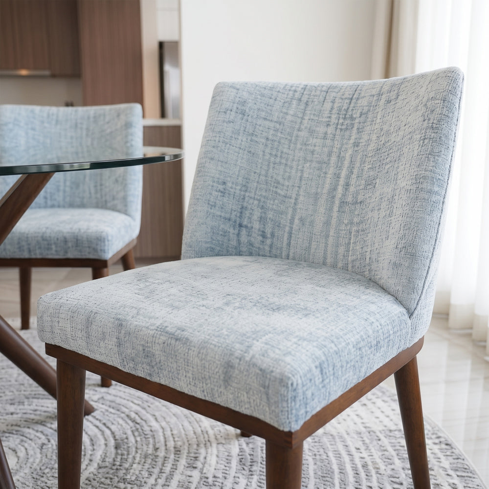 Grey dining chair in the foreground with a second chair and glass table behind it