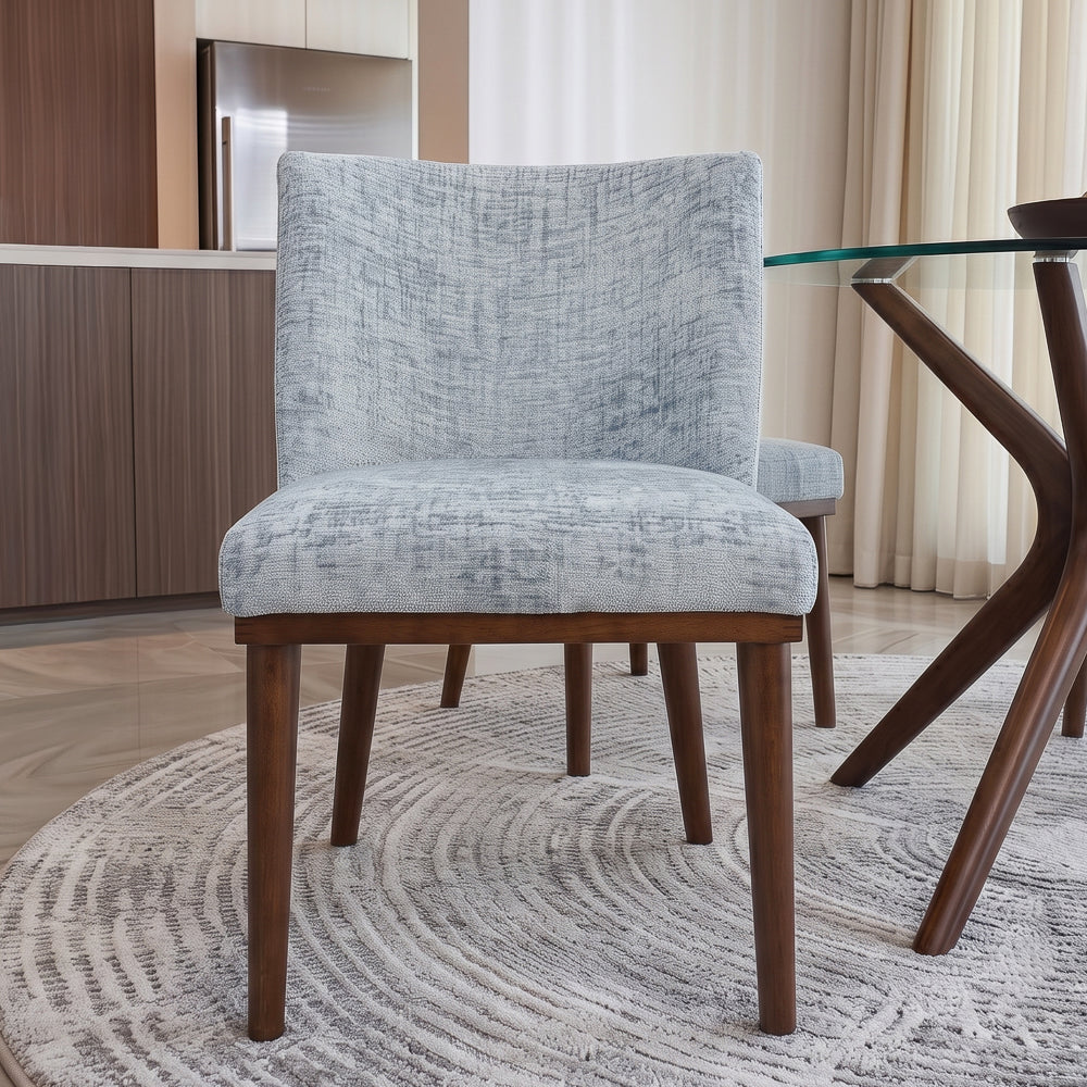 Front view of a grey dining chair tucked under a glass table on a textured round rug