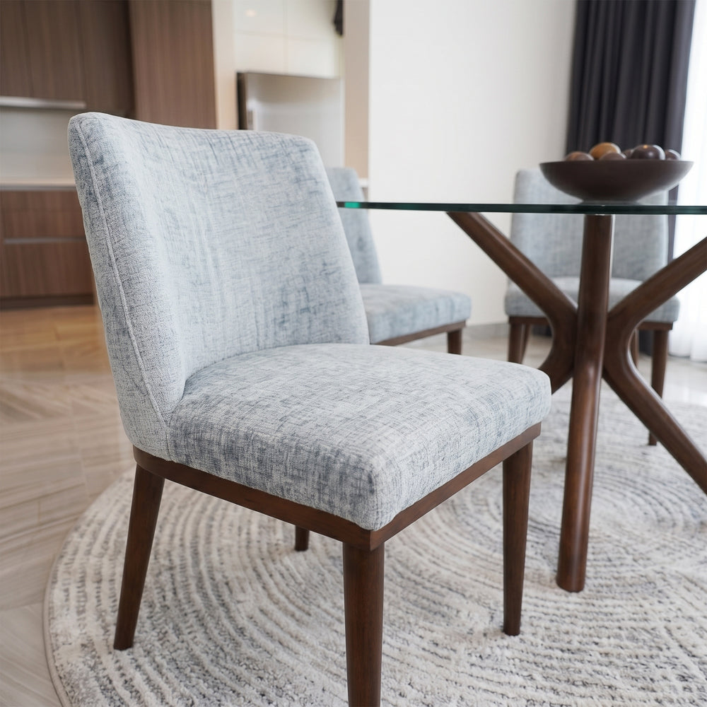 Angled close view of a grey dining chair by a glass table with a bowl of fruit