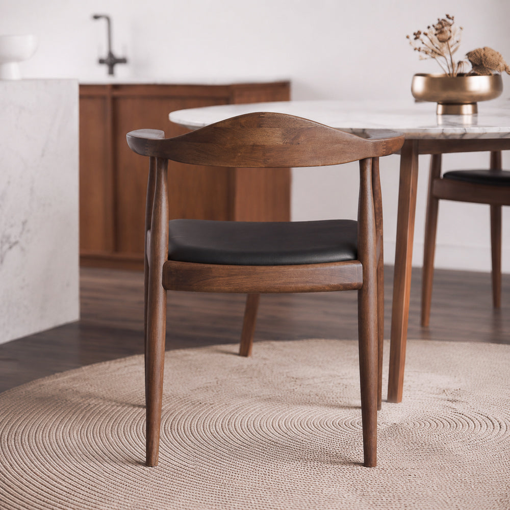 Rear view of the Freya chair showing its curved walnut backrest beside a round marble dining table