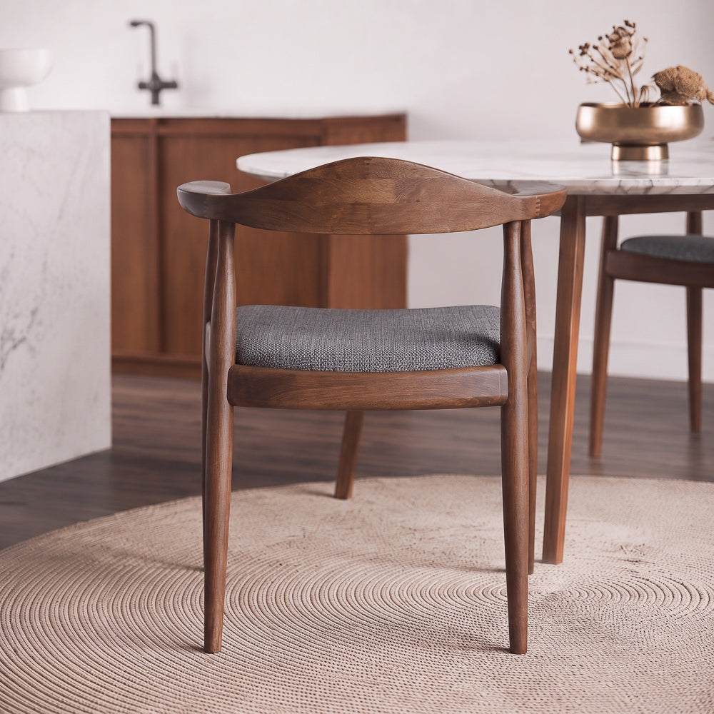 Rear view of Freya dining chair showing the curved walnut backrest and grey seat at a marble table.