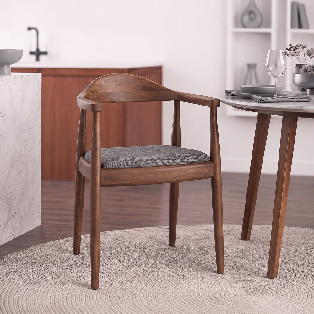 Freya dining chair in grey fabric, three-quarter front view beside a round marble dining table.