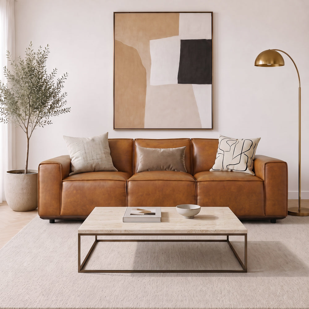 Living room with tan leather sofa, three accent cushions and a travertine coffee table
