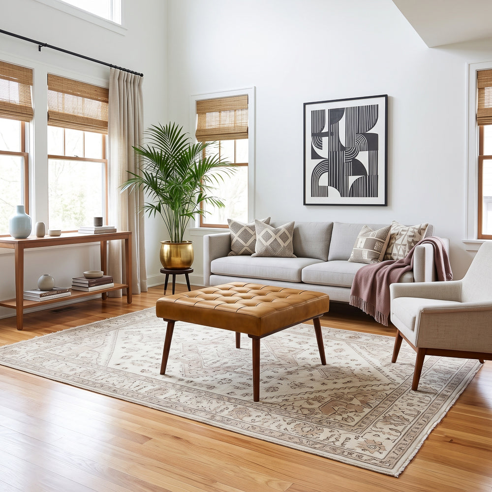 Wide living room view with the tan leather ottoman as a coffee table between a gray sofa, armchair, and windows.