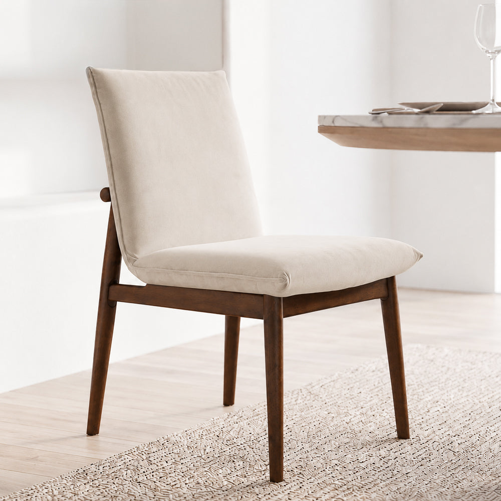 Angled view of a beige velvet dining chair next to a wood dining table with a place setting