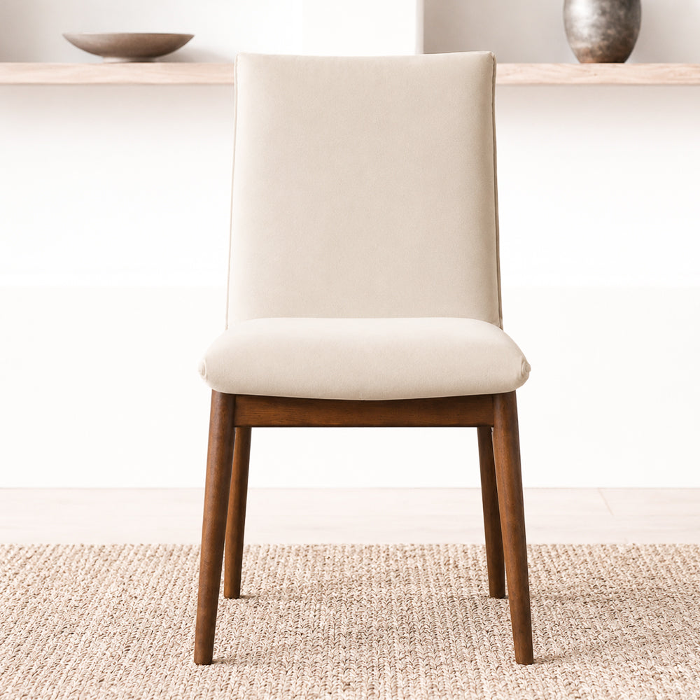 Front view of one beige velvet dining chair on a woven rug in front of a light wood console