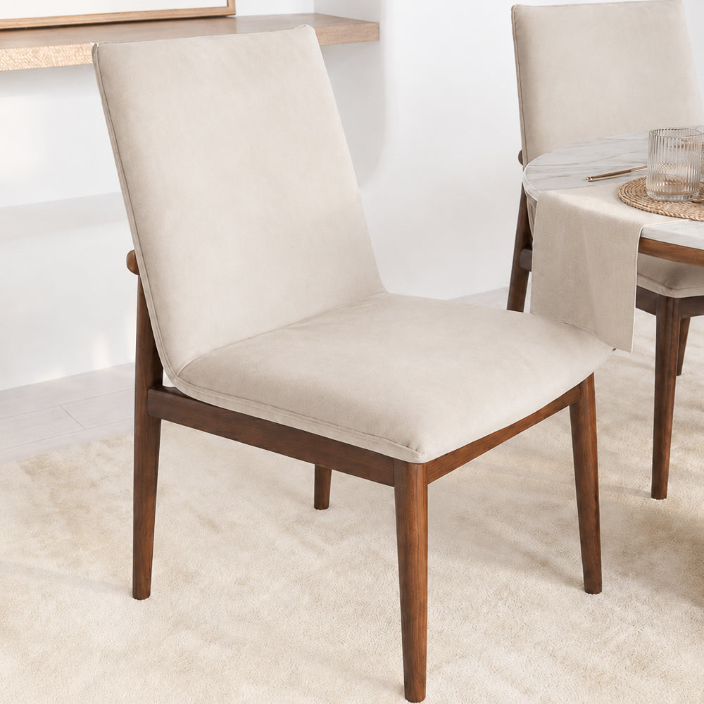 Close side view of a beige velvet dining chair beside a set table, showing padded seat and tapered legs