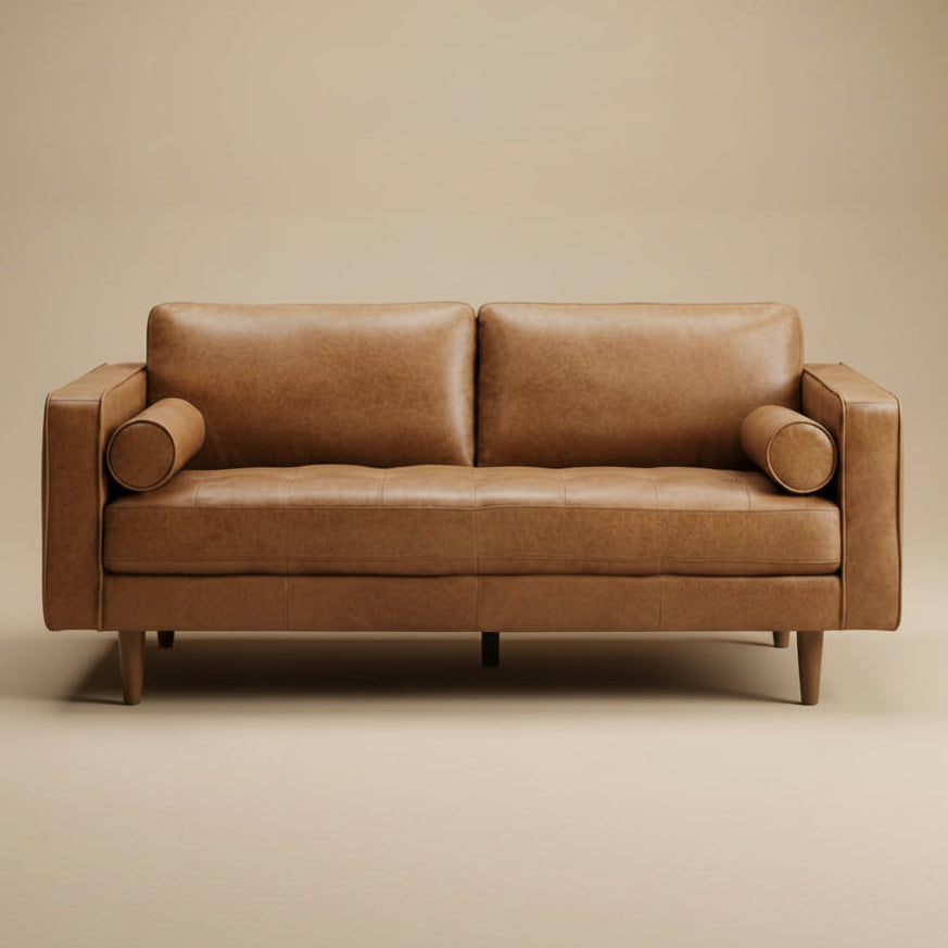 Tan leather compact sofa shown head-on against a beige studio backdrop with bolster pillows and tapered wood legs
