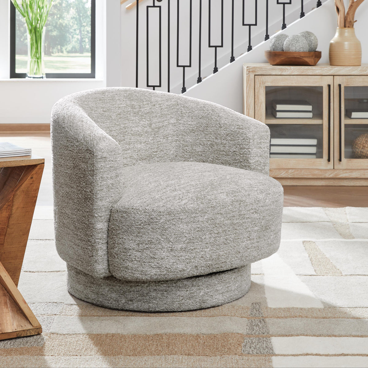 Gray swivel chair in a living room setting with a staircase and decor elements.