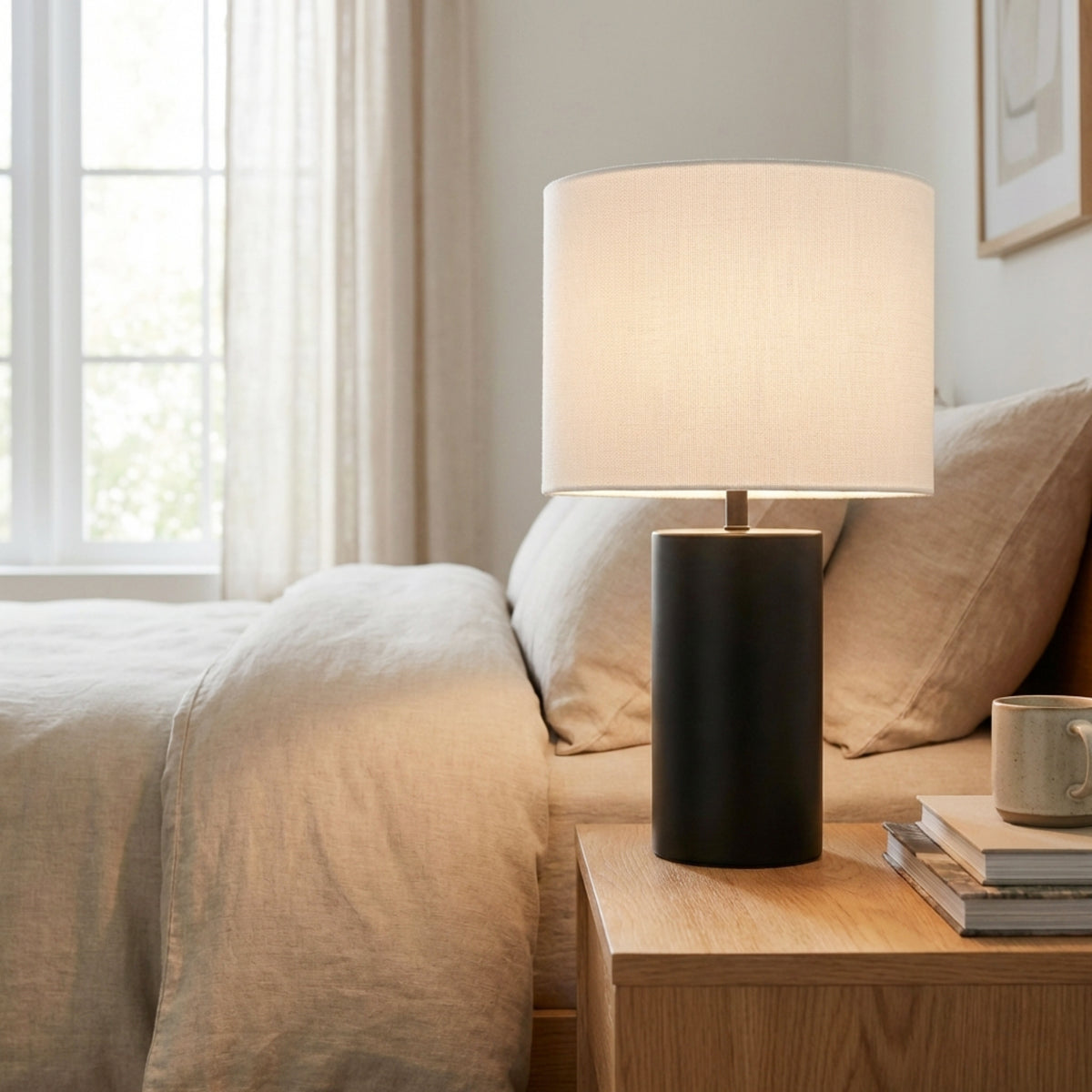 Lit black Table Lamp glowing on a wood nightstand next to a bed and bright window