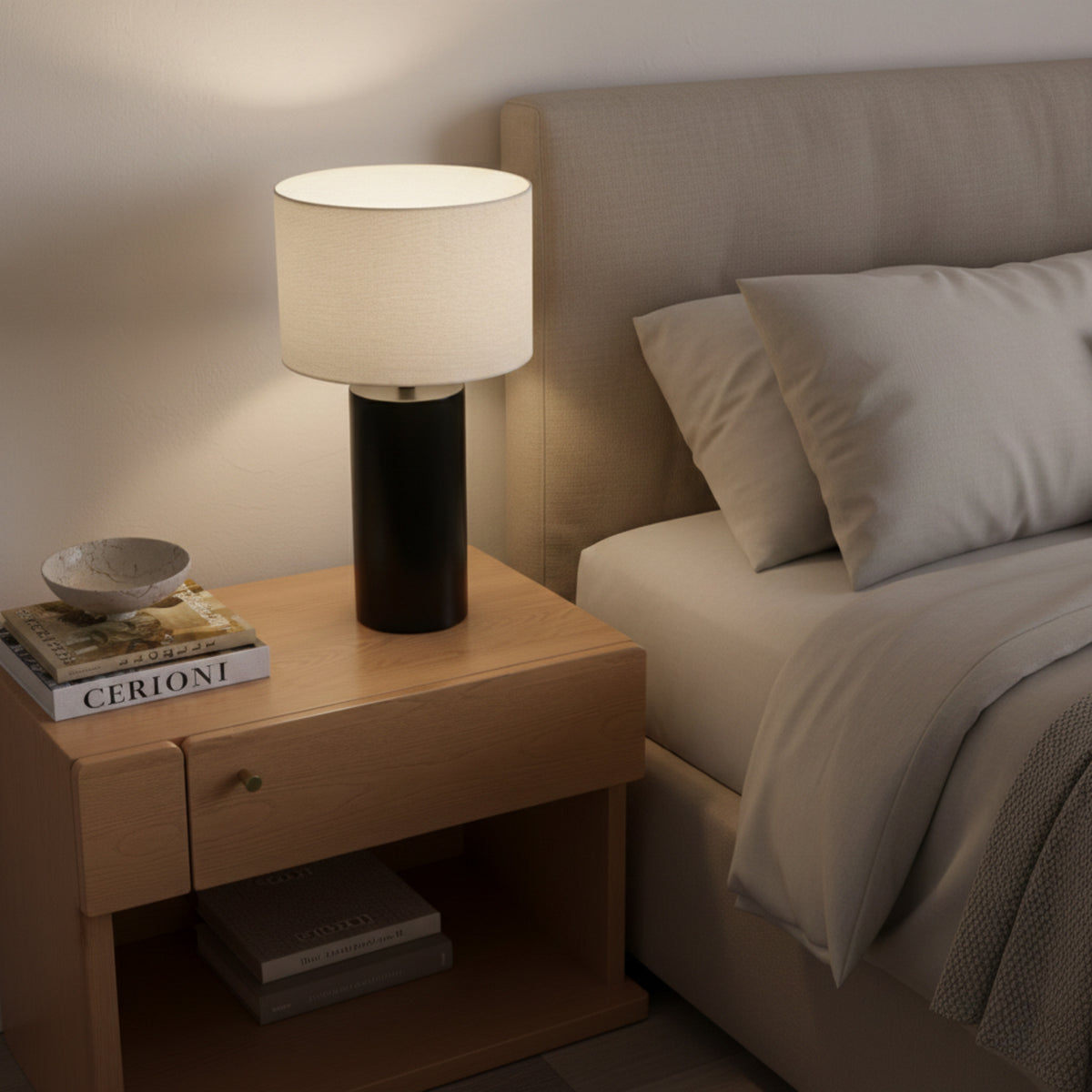 Angled bedside view of the lit Table Lamp on an oak nightstand with books on its lower shelf