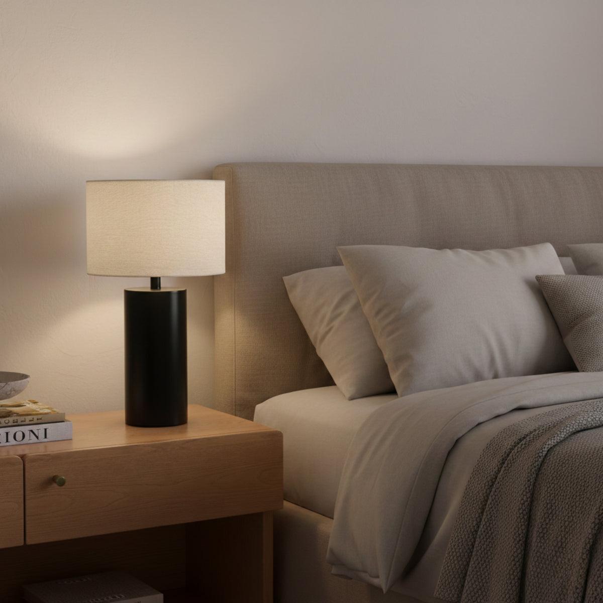 Table Lamp casting a warm glow up the wall beside an upholstered headboard and grey bedding