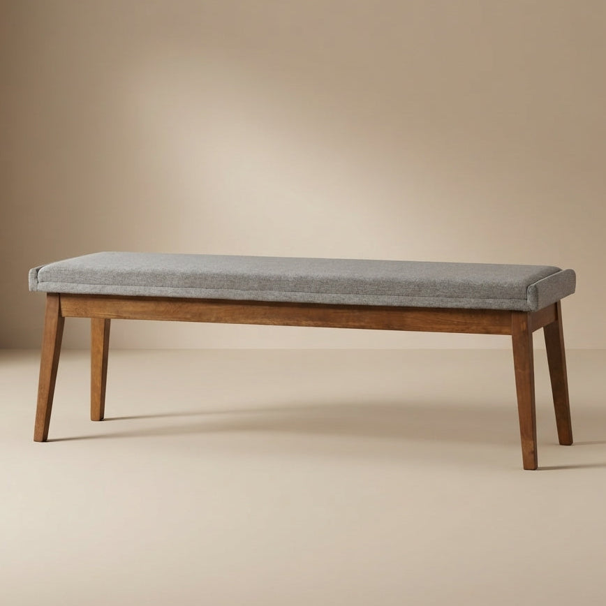 A wooden bench with a light gray upholstered seat cushion, shown in a clean studio setting with a warm beige background.