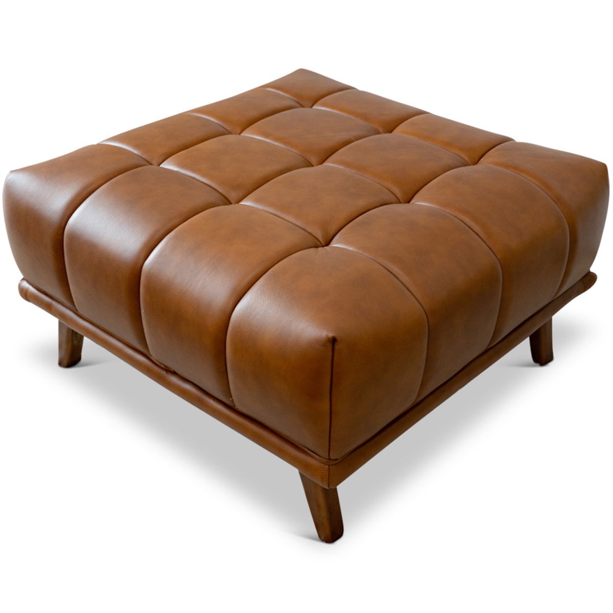 Isolated three-quarter shot of the cognac tufted leather ottoman with wood legs against a plain white background.