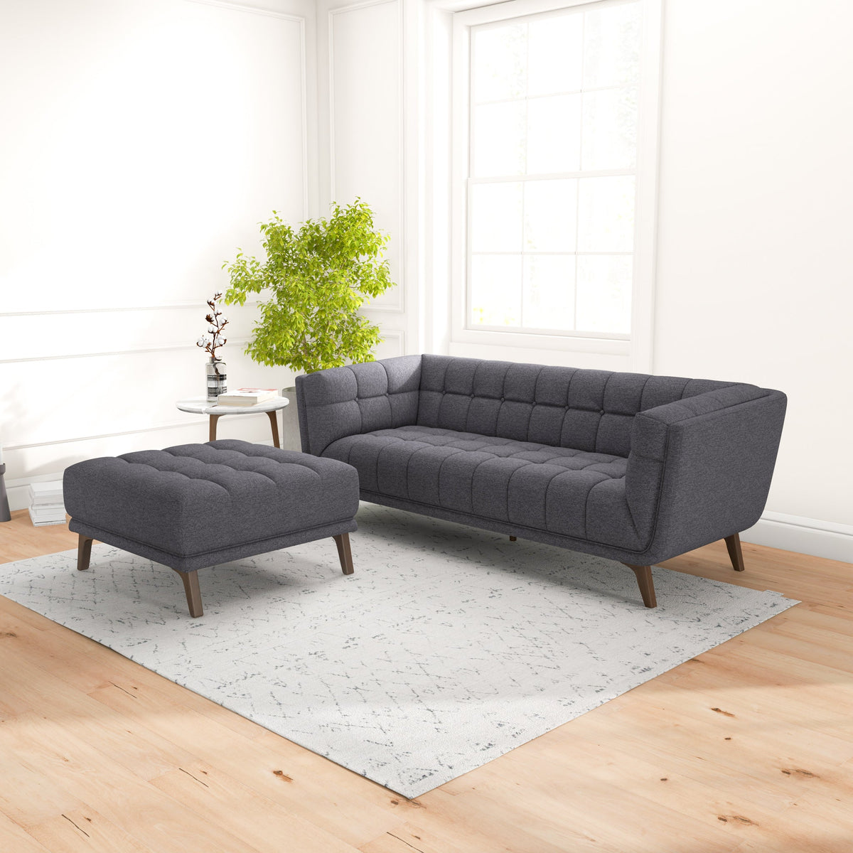 Living room with matching dark gray tufted sofa and ottoman on a pale rug, green plant, and a large window behind.