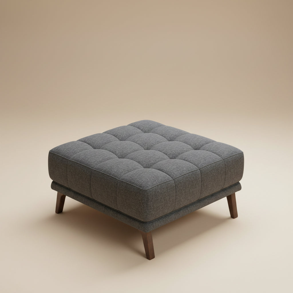 Square dark gray tufted fabric ottoman with four tapered wood legs, isolated on a seamless beige studio background.
